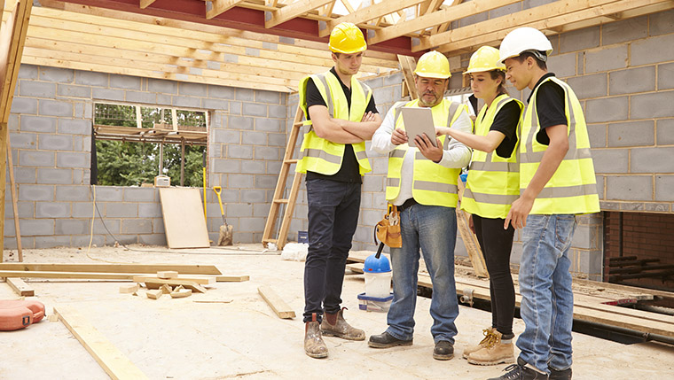 Builder On Site Looking At Digital Tablet With Apprentices